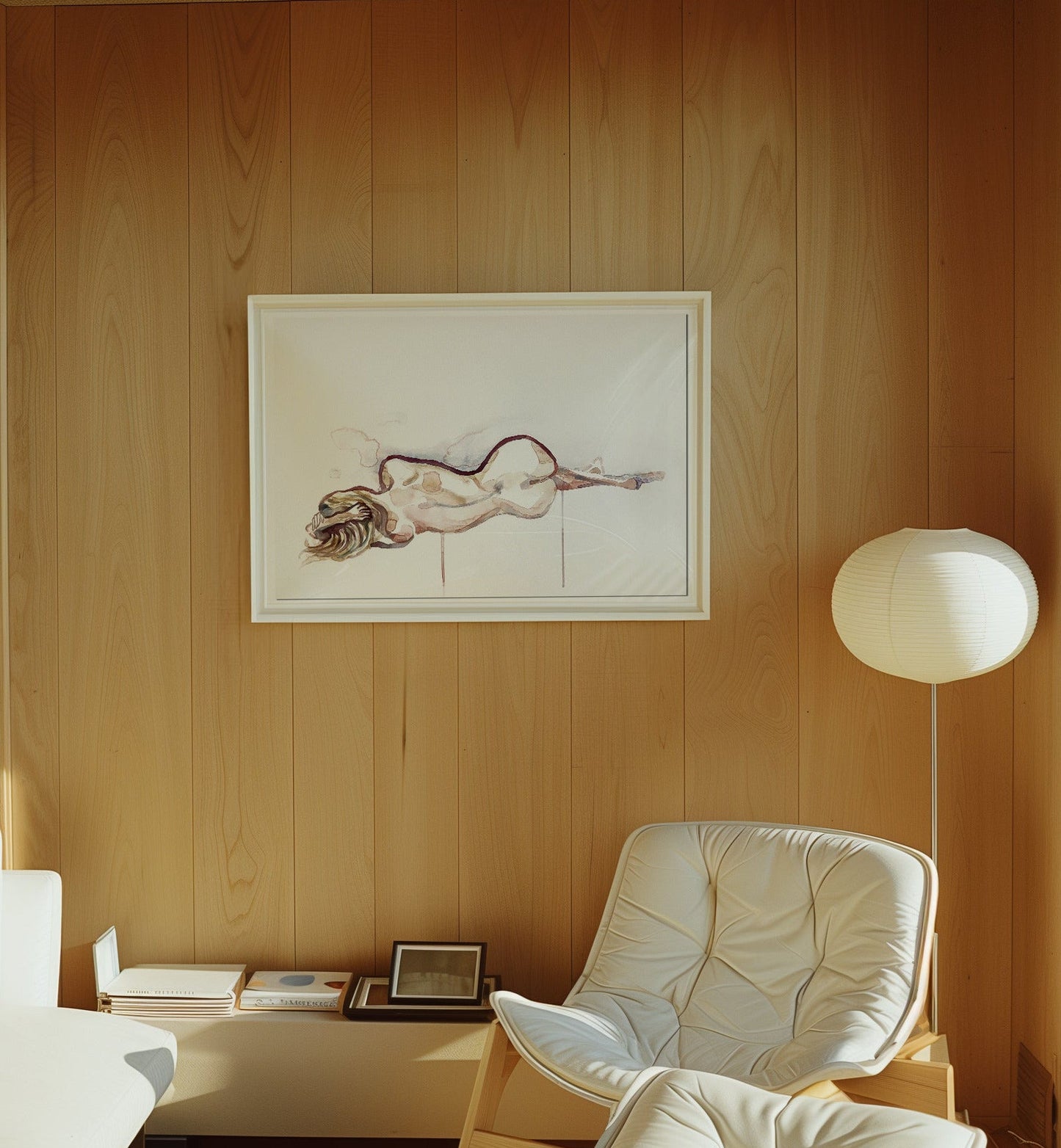 A watercolor painting featuring a nude minimalist figure hanging on a warm wood-paneled wall in a design-focued, sunlit living room with a mid-century white armchair and floor lamp.