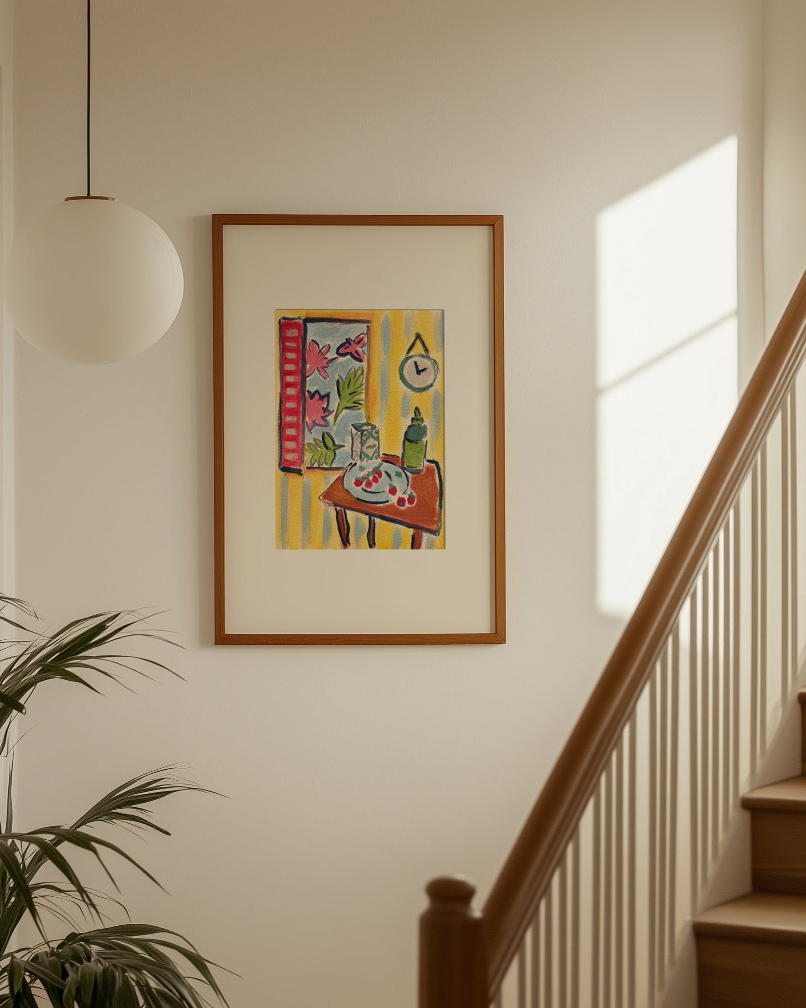 Framed artwork on a wall above a staircase with a plant to the left.