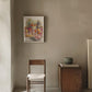 Room interior with a chair, small table, and framed artwork on a beige wall.