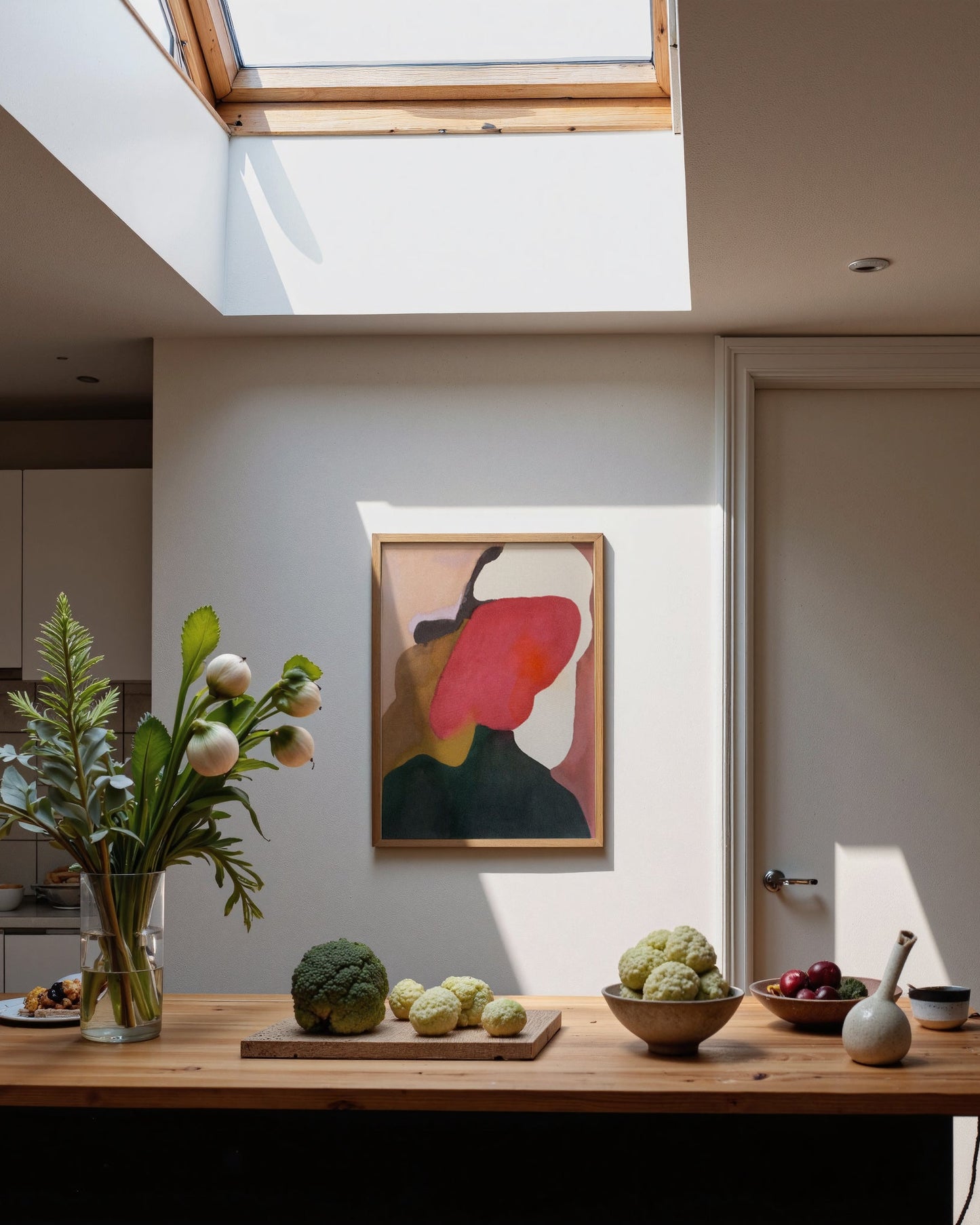 Modern kitchen with wooden table, plants, and abstract art on the wall.