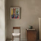 Room interior with a chair, small table, and framed artwork on a beige wall.