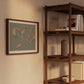 Framed abstract art on a wall next to a wooden bookshelf with books and decor items.