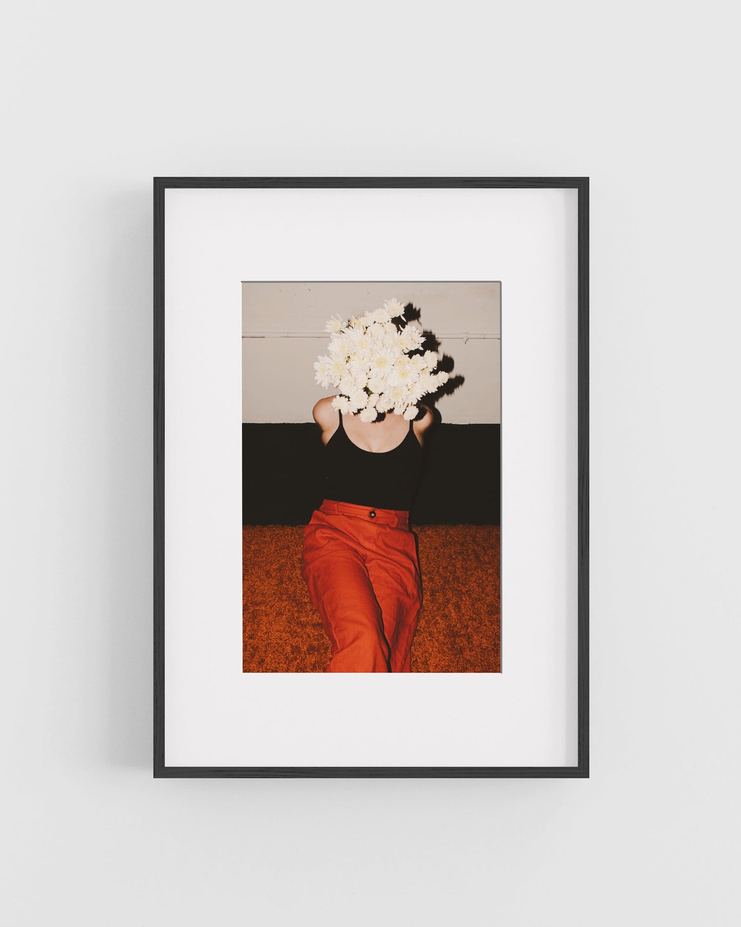 Framed artwork of a person with flowers covering their face on a plain wall.