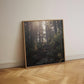 Framed photograph of a forest leaning on a wall in a room with wooden flooring.