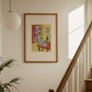Framed artwork on a wall above a staircase with a plant to the left.