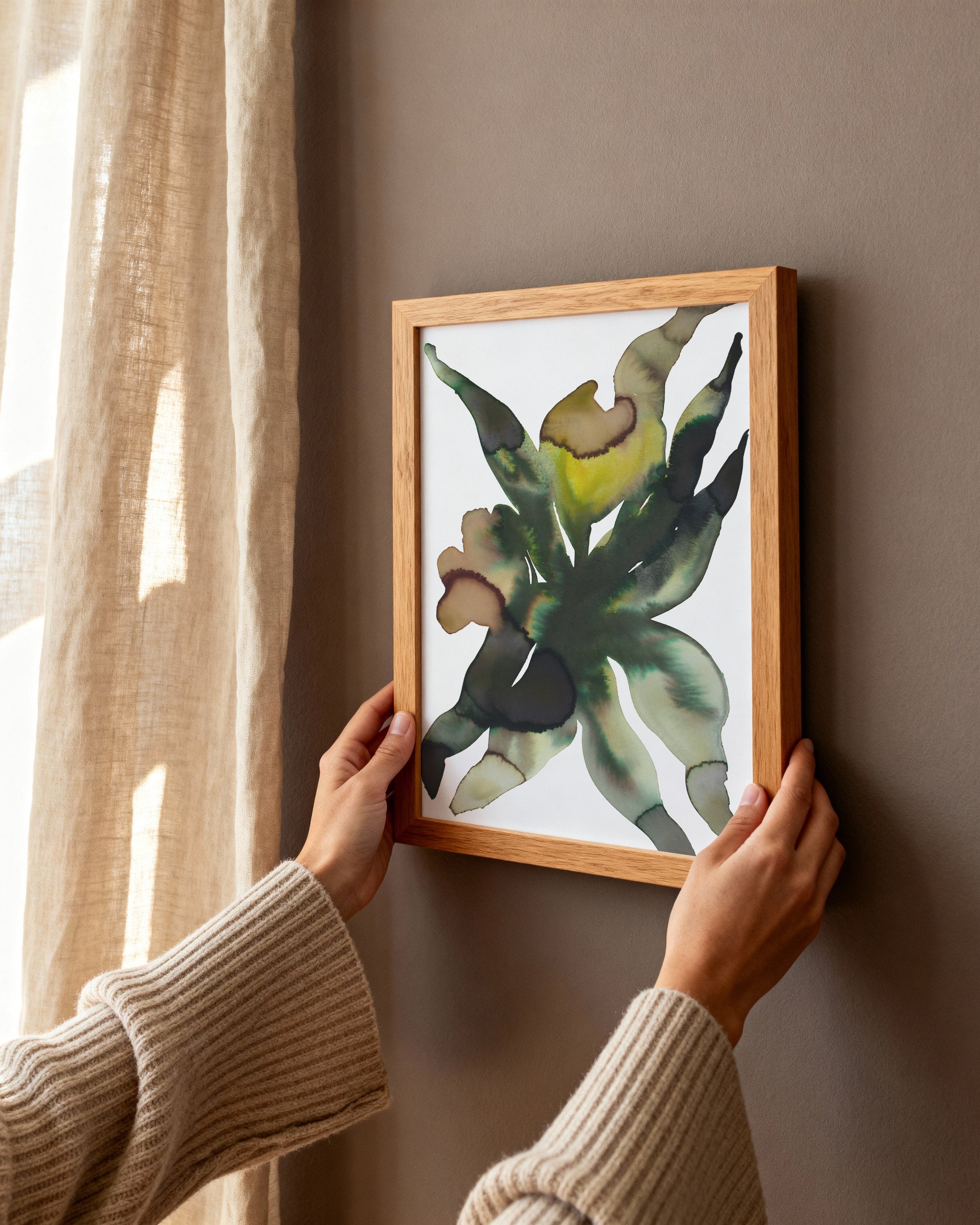 Person hanging a framed artwork of an abstract flower on a wall.