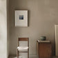 Minimalist room with a wooden chair, small table, and framed picture on a beige wall.