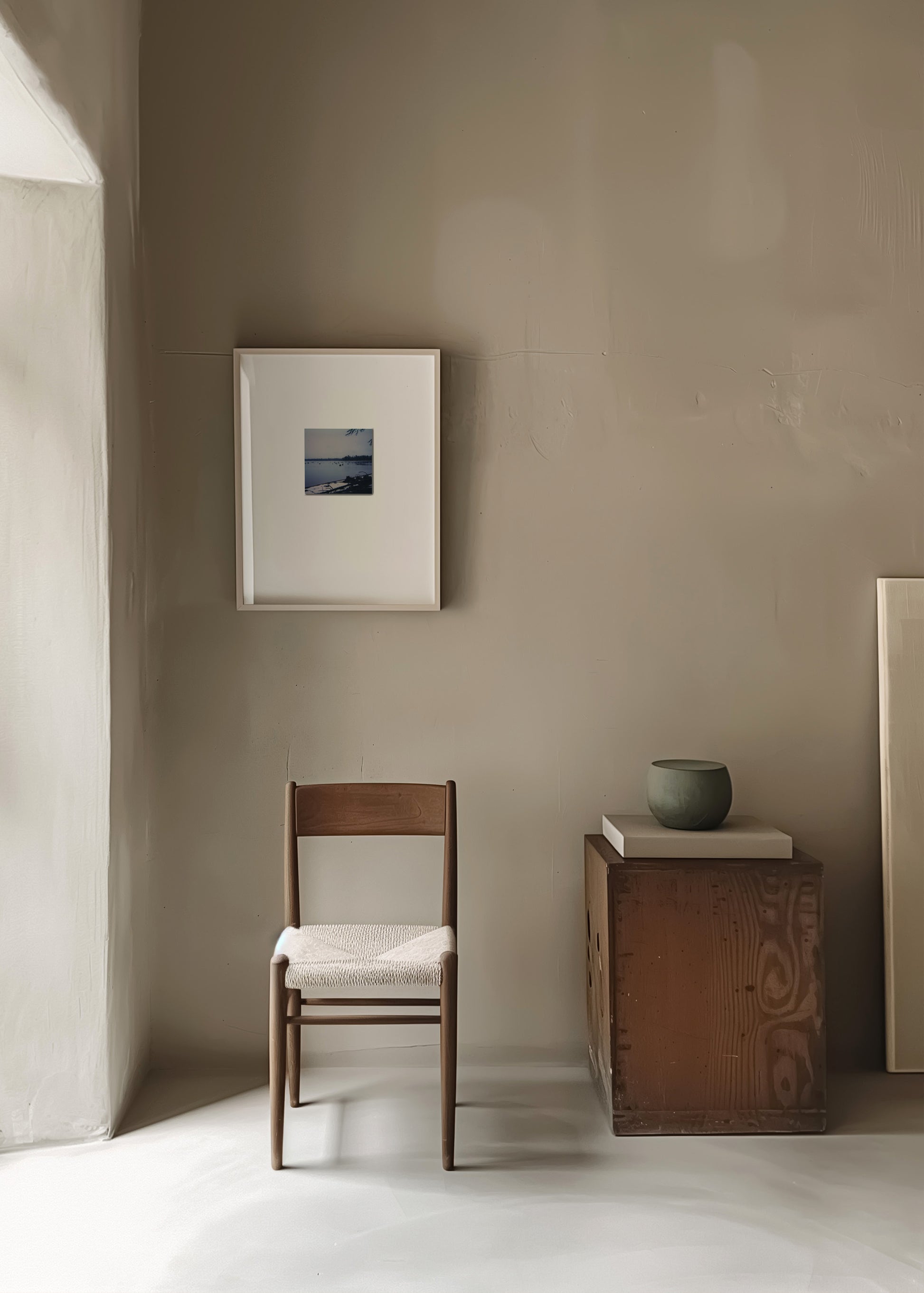 Minimalist room with a wooden chair, small table, and framed picture on a beige wall.