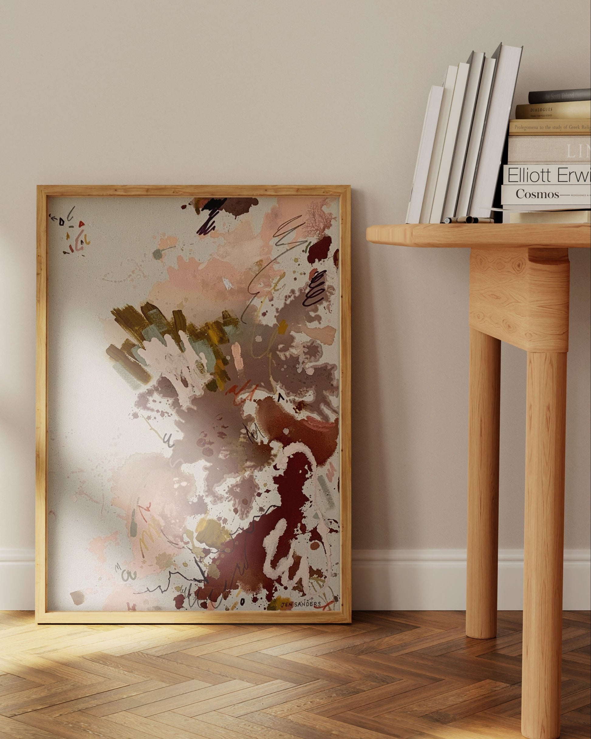 Framed abstract art leaning on a wall next to a wooden desk. 