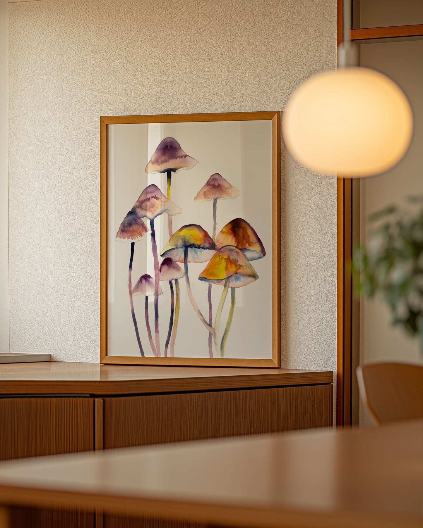 Framed artwork of colorful mushrooms on a wall in a room with wooden furniture and a lamp.