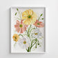 Framed floral artwork with yellow, pink, and white flowers on a white wall.