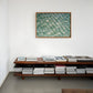 Wooden shelf with books and a framed photograph of water rippling sand on a white wall