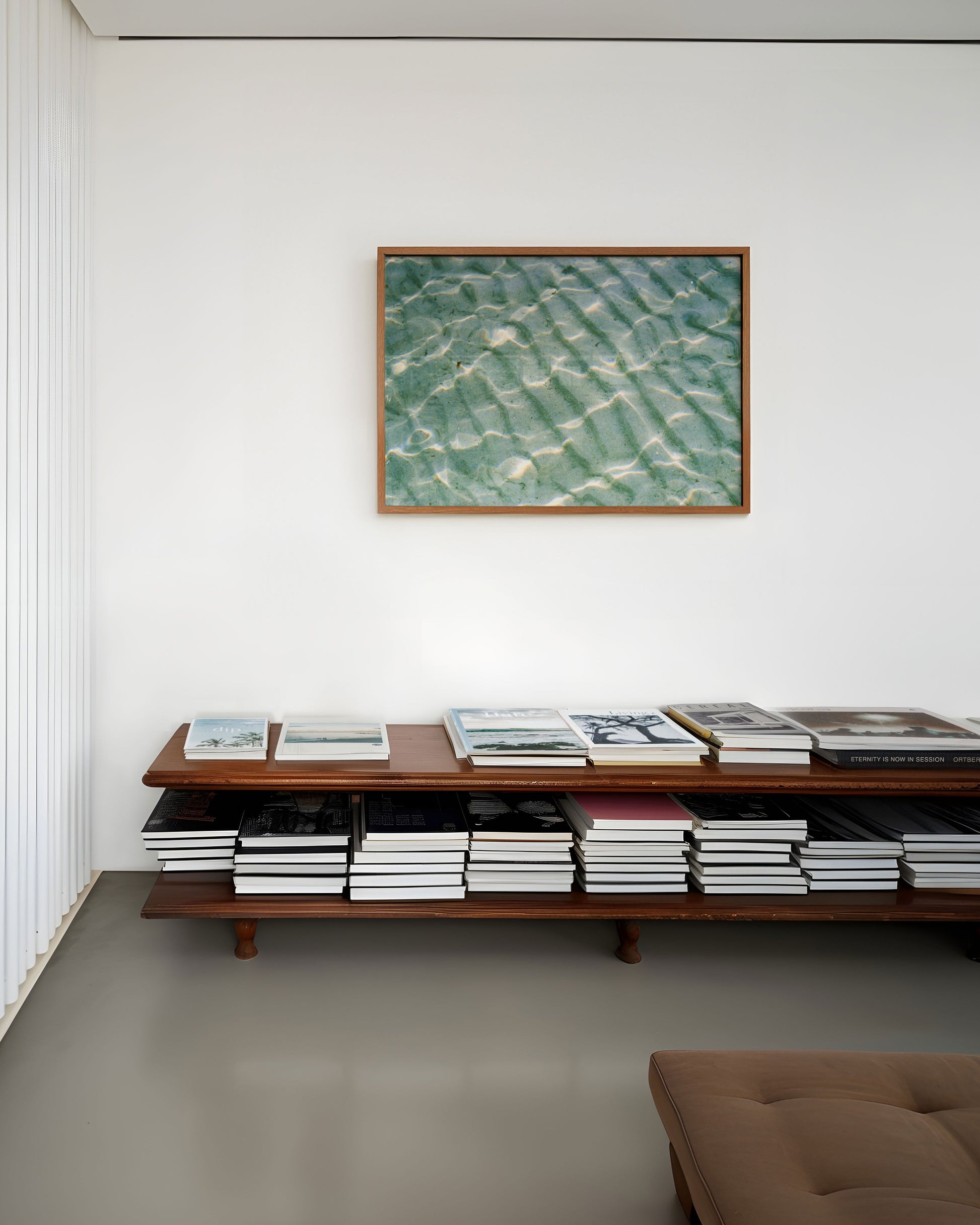 Wooden shelf with books and a framed photograph of water rippling sand on a white wall